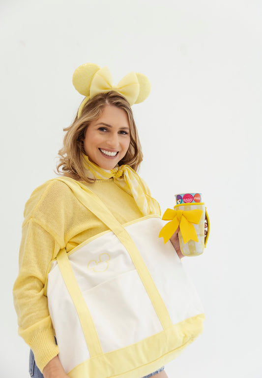 Woman in a yellow and white costume with a bow, holding a yellow and white striped cup coozie.