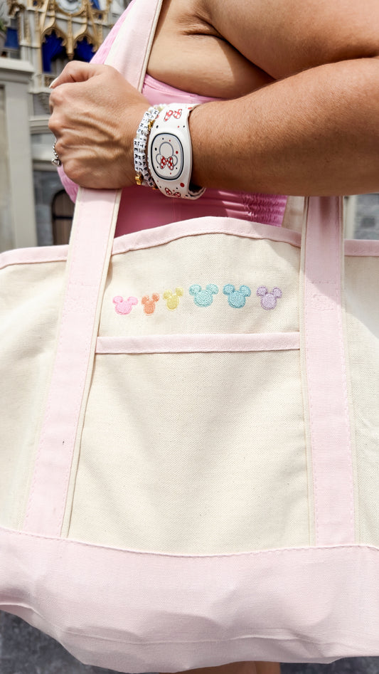 Person holding a light pink tote bag with cartoon character designs, wearing a wristwatch.