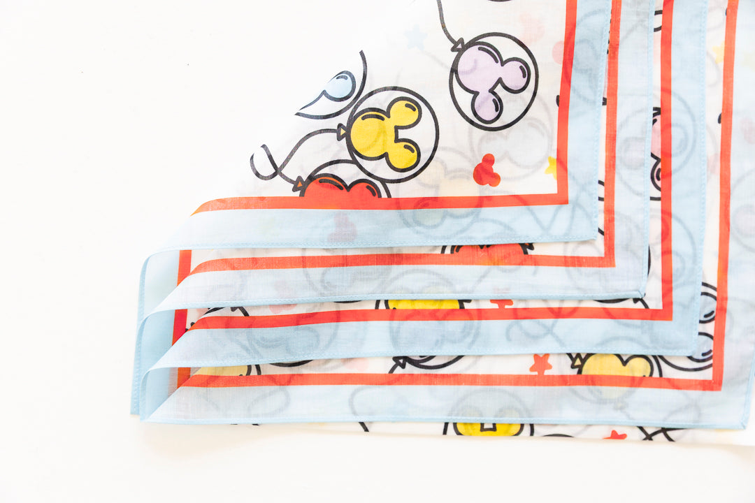 A folded square scarf with a light blue background, featuring a cartoon Mouse balloon print in yellow, red, and purple, framed by orange-red borders.