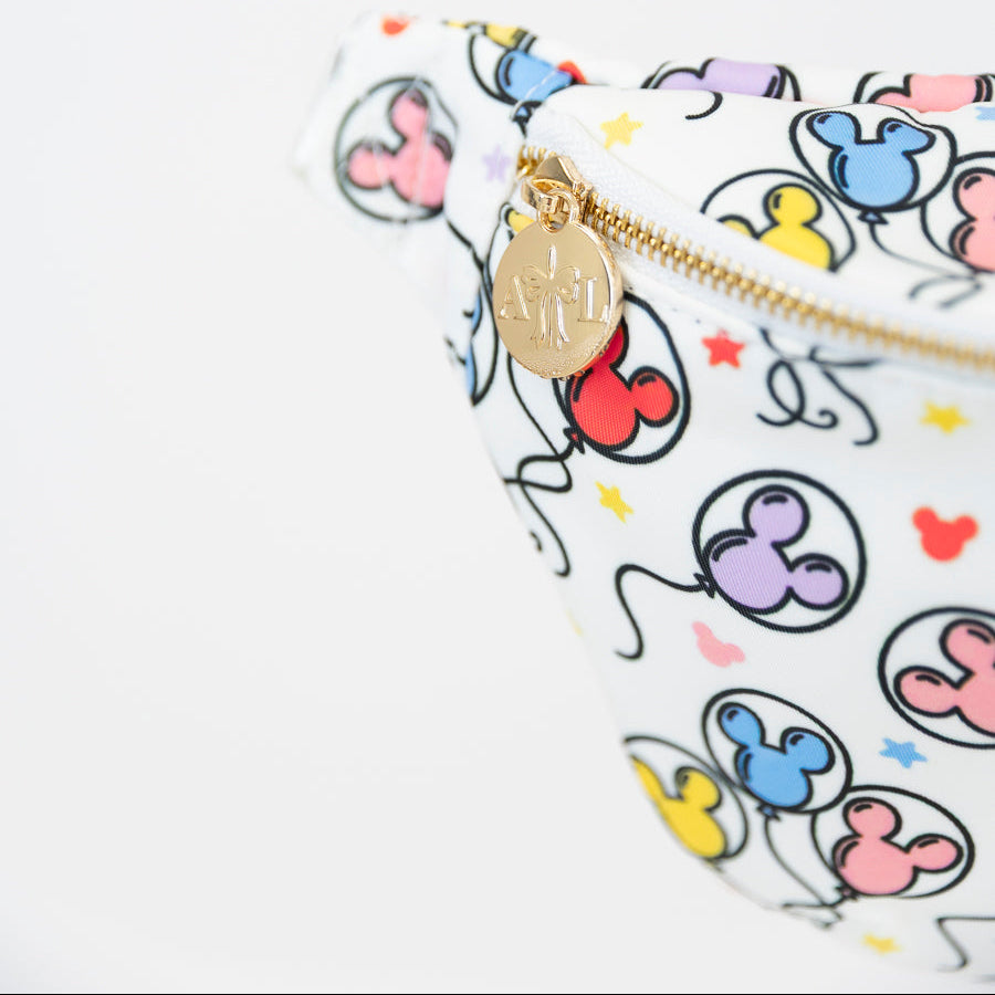 A close-up of a white fanny pack featuring a colorful cartoon balloon print and a gold-tone zipper with a round metal charm.