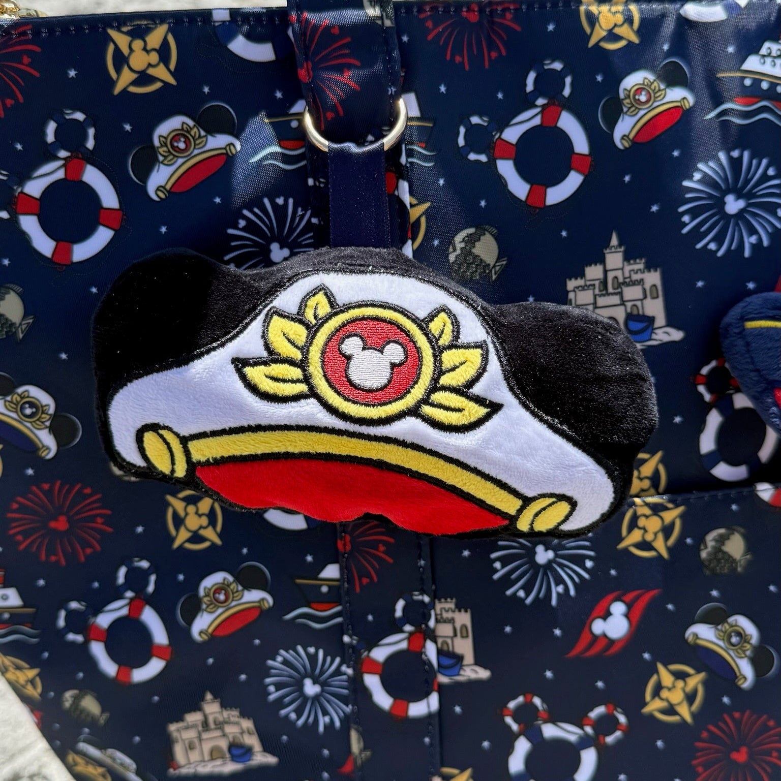 Nautical-themed bag with a plush bag charm shaped like Mouse's captain hat on a sandy background
