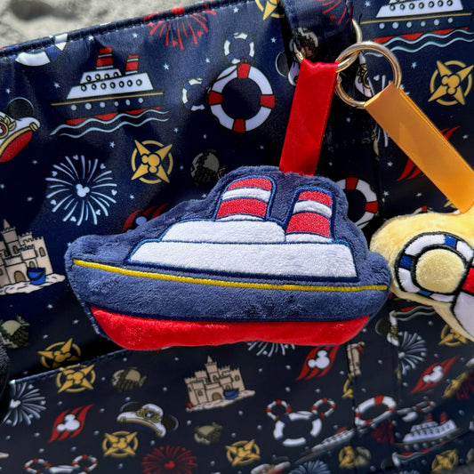 Tote bag with nautical-themed design and toy ship attached, on a textured surface.