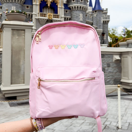 Pink backpack with colorful mouse heads held in front of a castle.