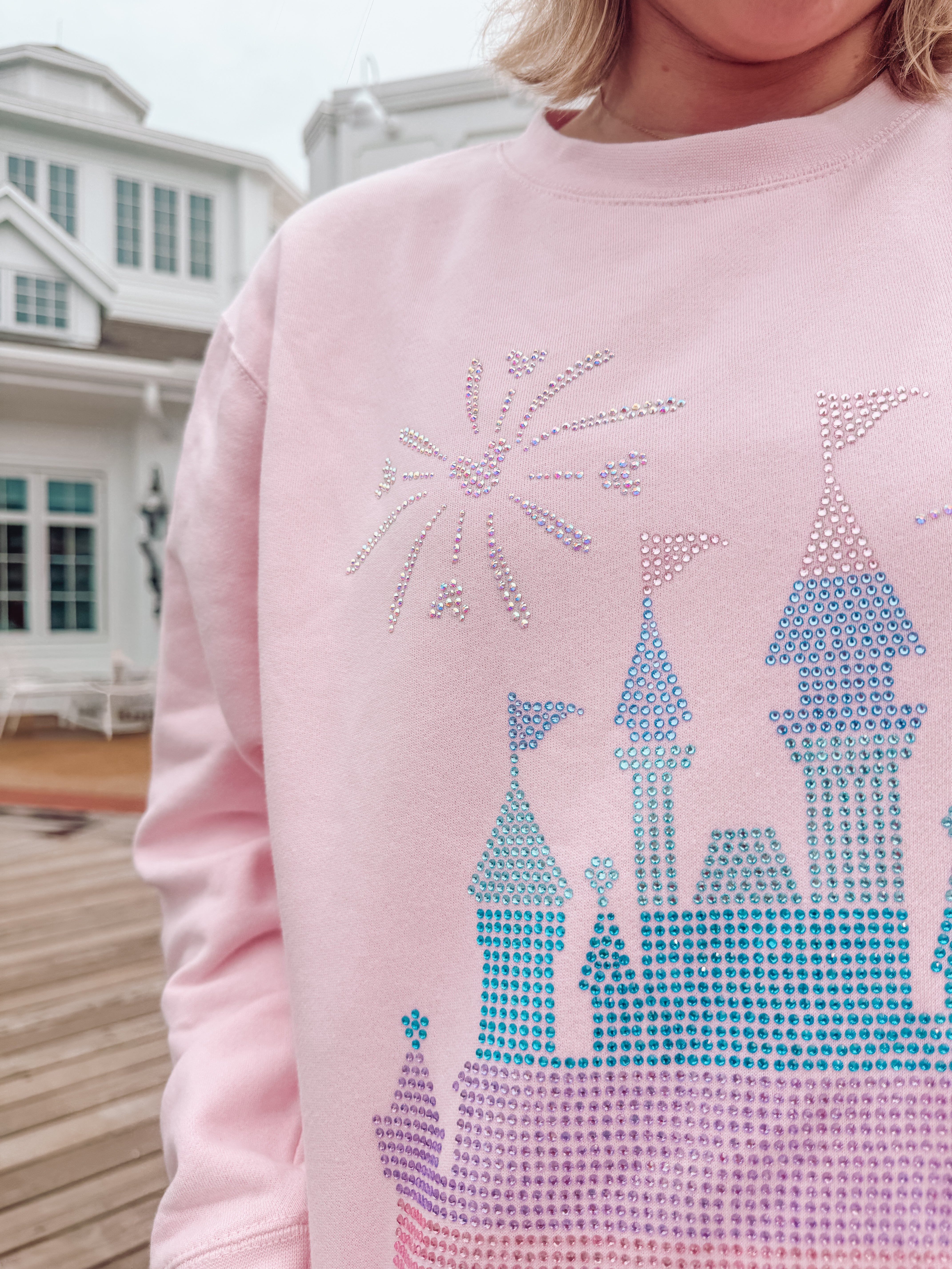 Pink sweatshirt with a castle design made of rhinestones, worn by a person.