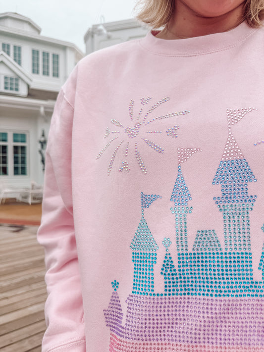 Pink sweatshirt with a castle design made of rhinestones, worn by a person.