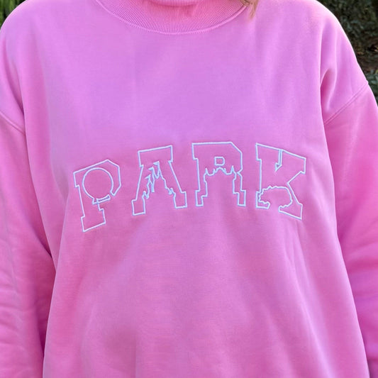 Person wearing a pink sweatshirt with 'PARK' text, white shorts, and pink mouse ears outdoors.