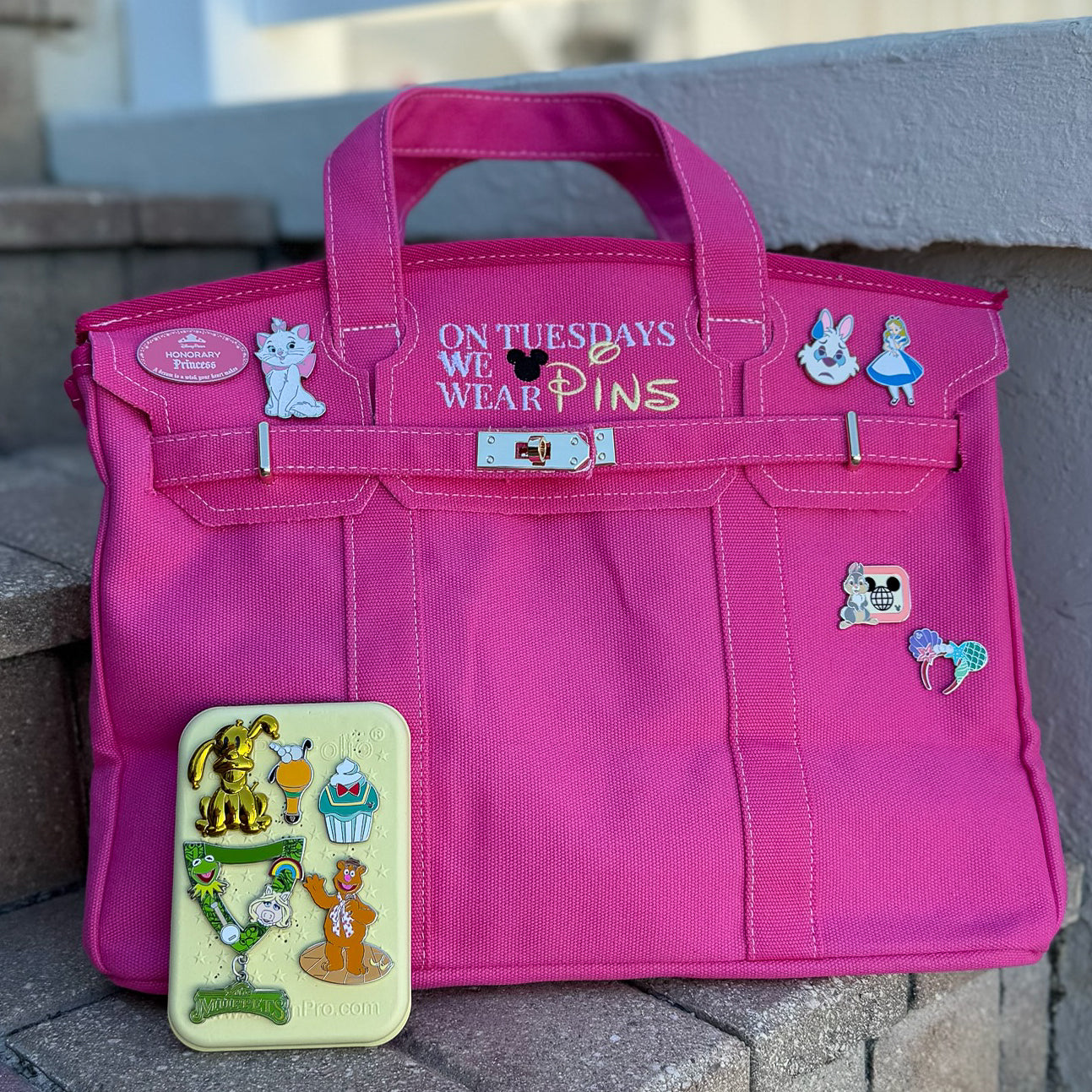 Pink bag with Disney pins on a stone surface