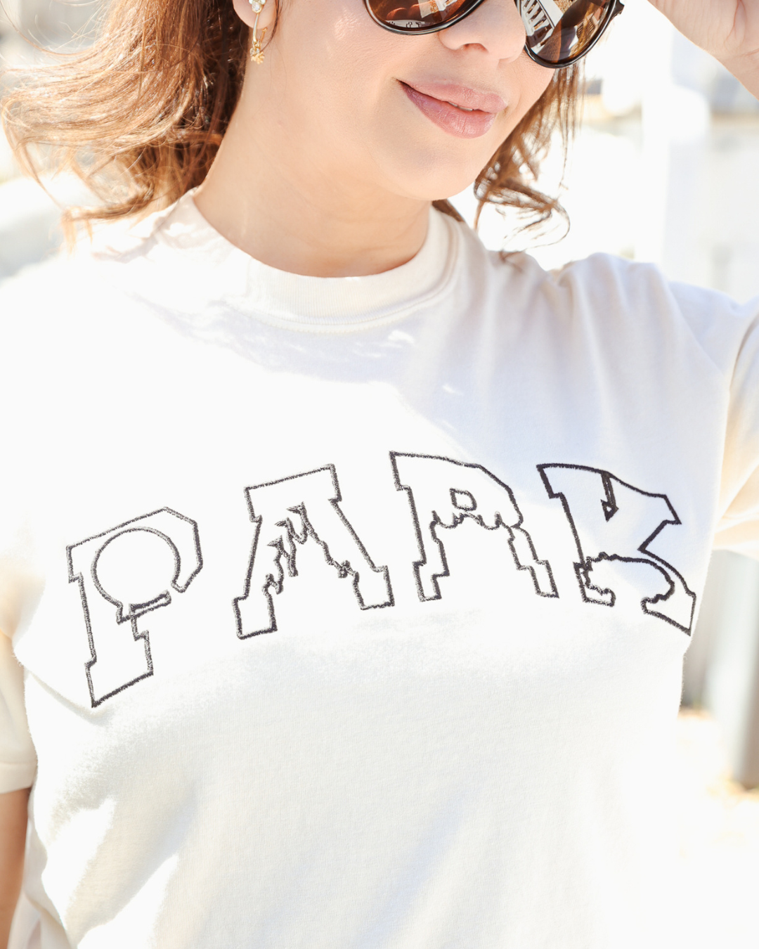 Person wearing a white t-shirt with 'PARK' printed on it, outdoors.