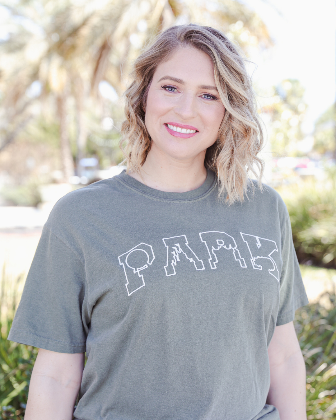 Woman wearing a green t-shirt with 'PARK' printed on it, standing outdoors.