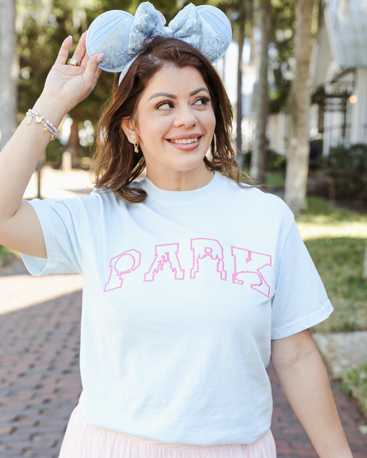 Woman wearing a light blue t-shirt with 'PARK' printed on it, holding up a plush toy.