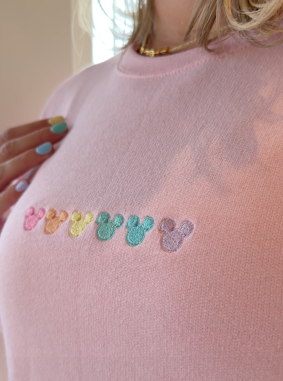 Colorful mouse ears embroidered on a light pink sweatshirt.
