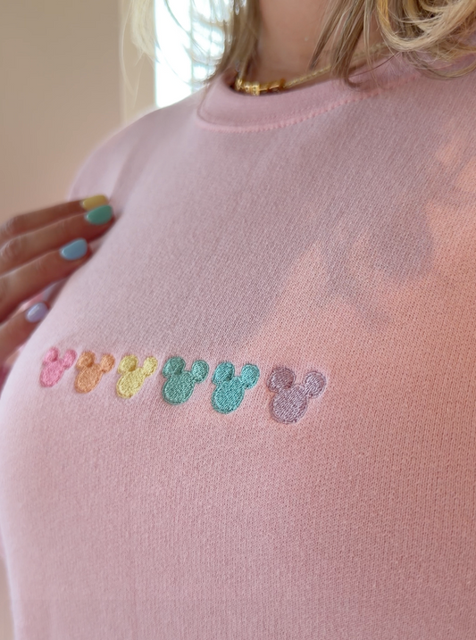 Colorful mouse ears embroidered on a light pink sweatshirt.