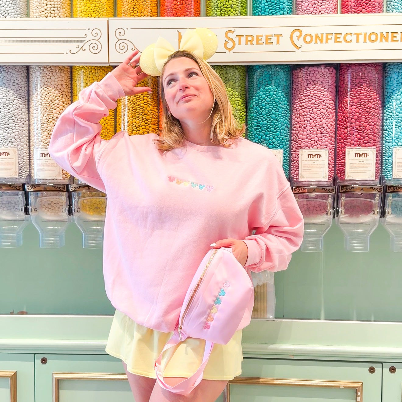 Person in a pink sweatshirt and yellow shorts standing in front of colorful candy display