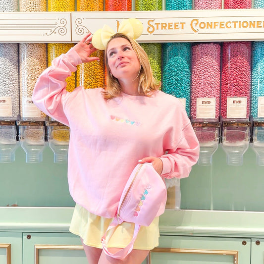 Person in a pink sweatshirt and yellow shorts standing in front of colorful candy display