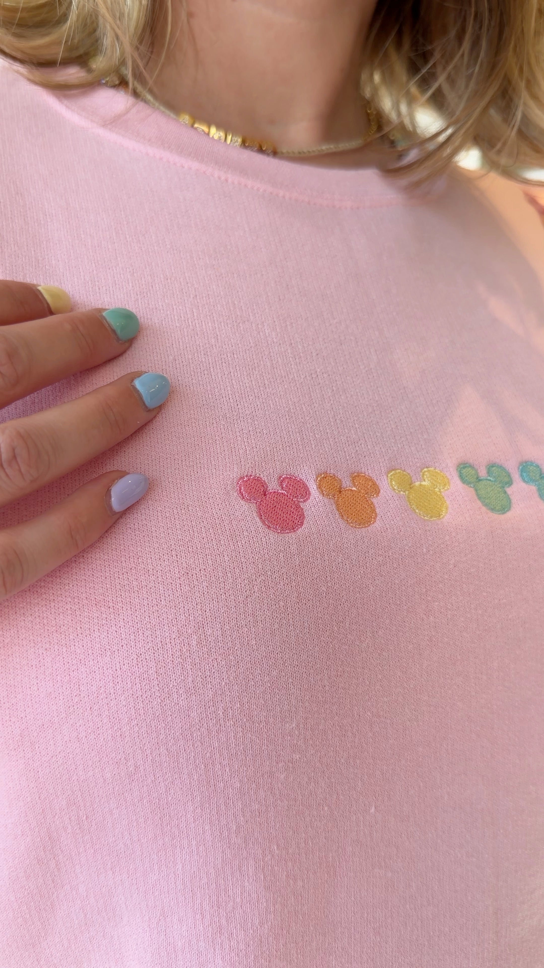 Close-up of a pink shirt with colorful mouse ears design and a hand with multicolored nails.