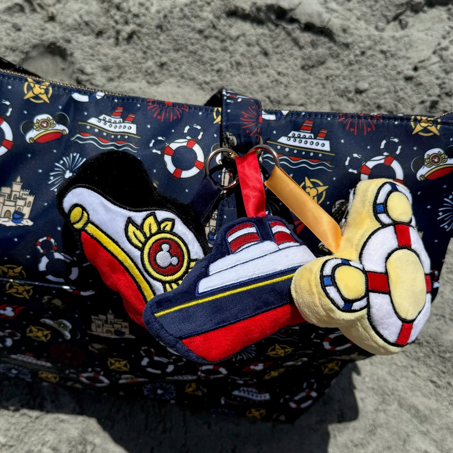 bag with nautical design and plush nautical bag charms on a sand background