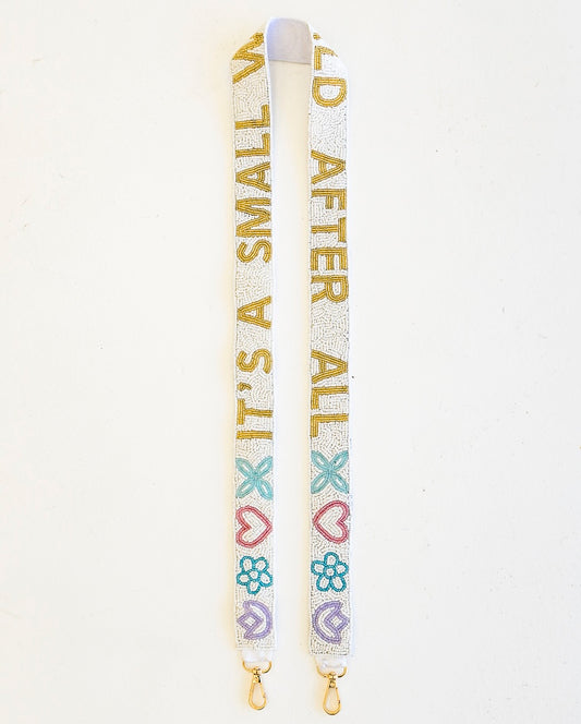 A white beaded purse strap with gold text reading 'IT'S A SMALL WORLD AFTER ALL' and decorated with pastel pink, blue, and purple hearts, flowers, and bows, shown on a plain white background.